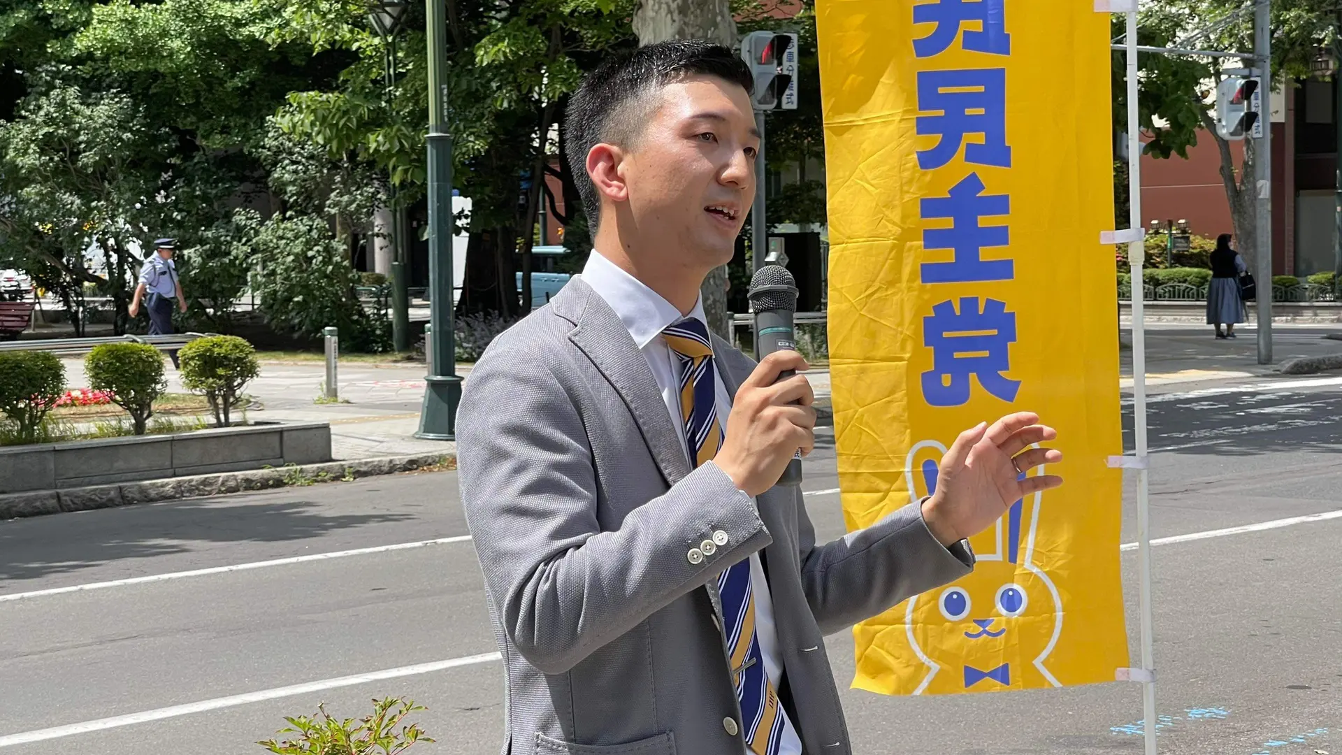 国民民主党ののぼりの前でマイクを持ち街頭で話す阿部恭介